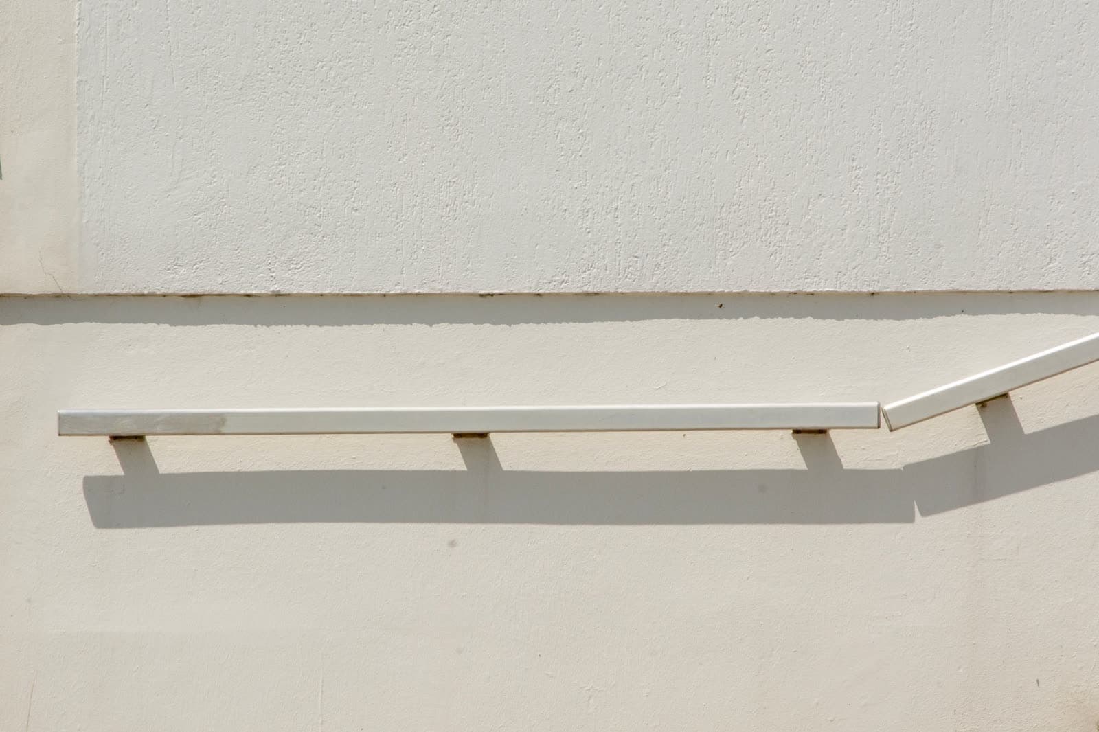 Pasamanos blanco sobre un muro claro con su sombra marcada