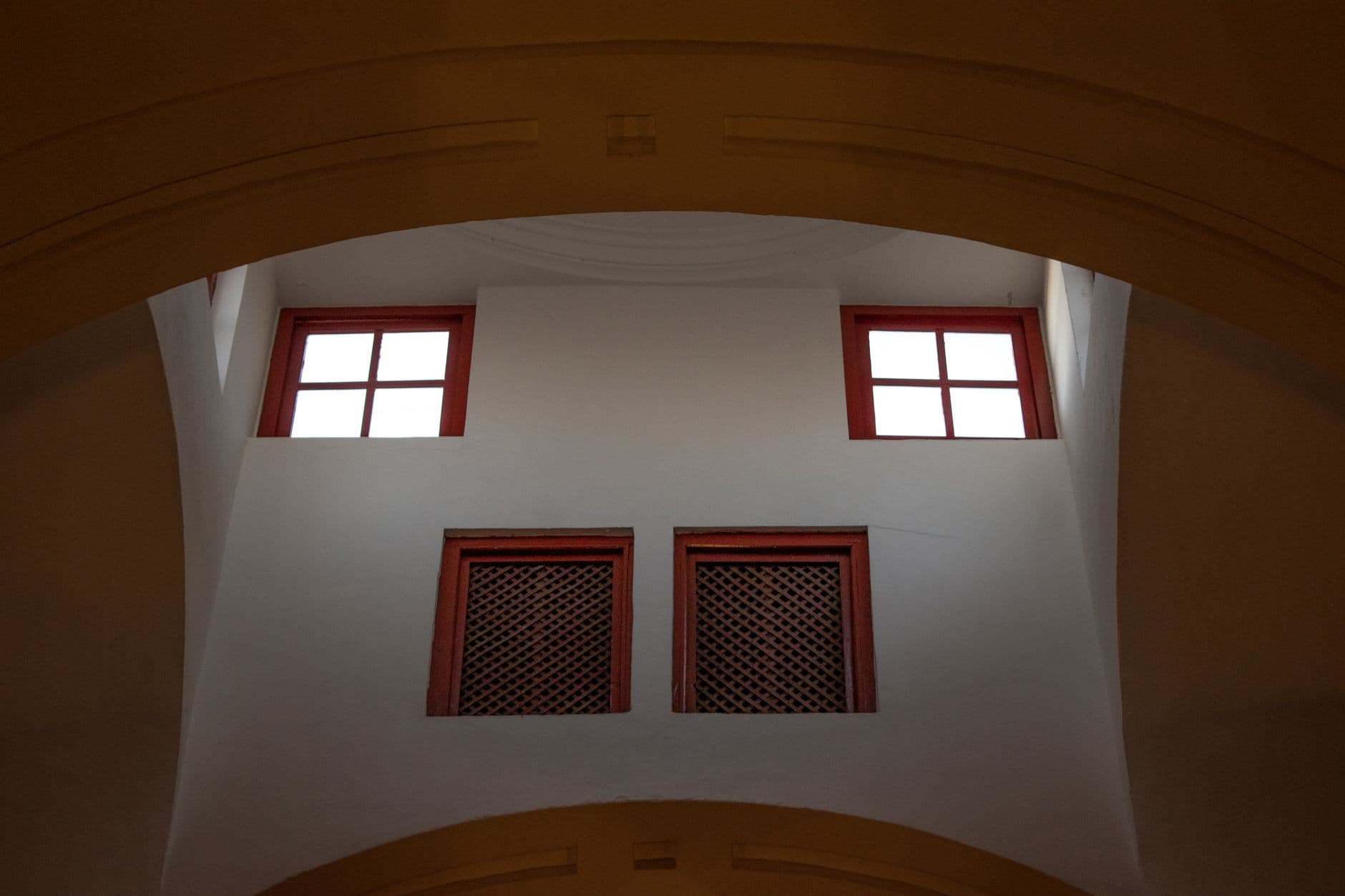 Ventanas altas y celosías de madera en un muro blanco, vistas desde abajo