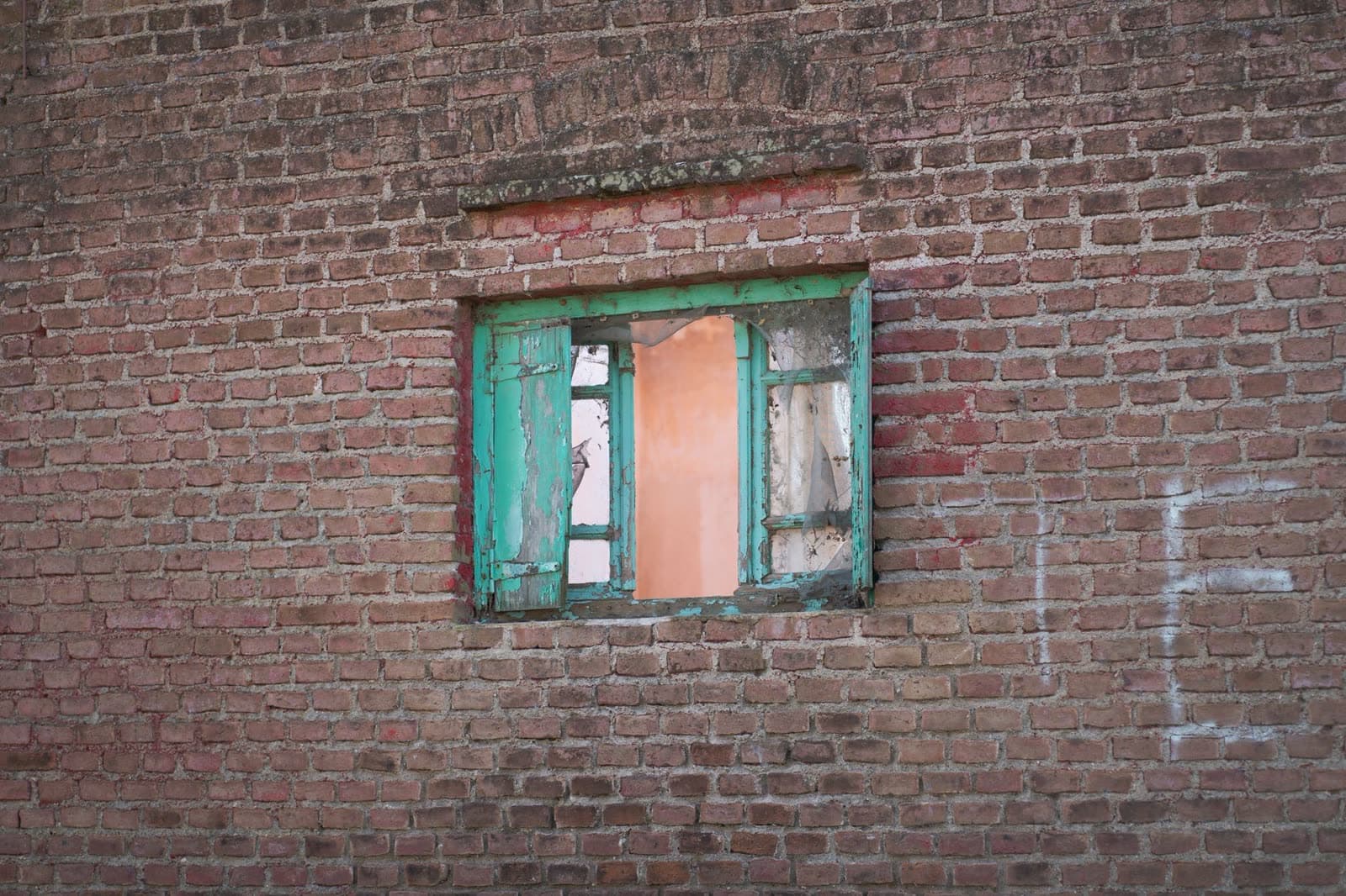 Muro de ladrillo con una ventana pequeña de carpintería verde desconchada