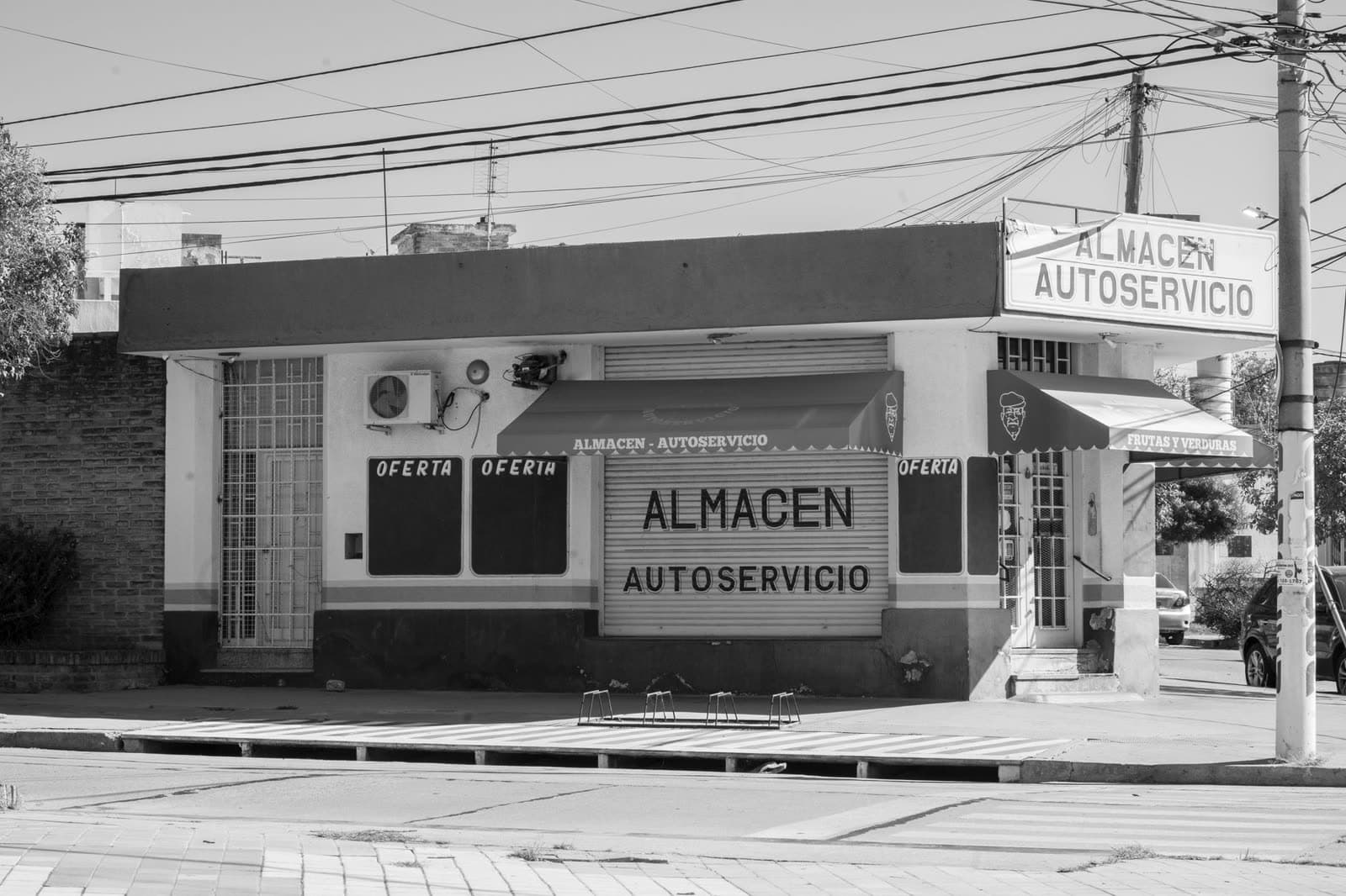 Comercio de esquina cerrado con el cierre metálico bajado, en blanco y negro