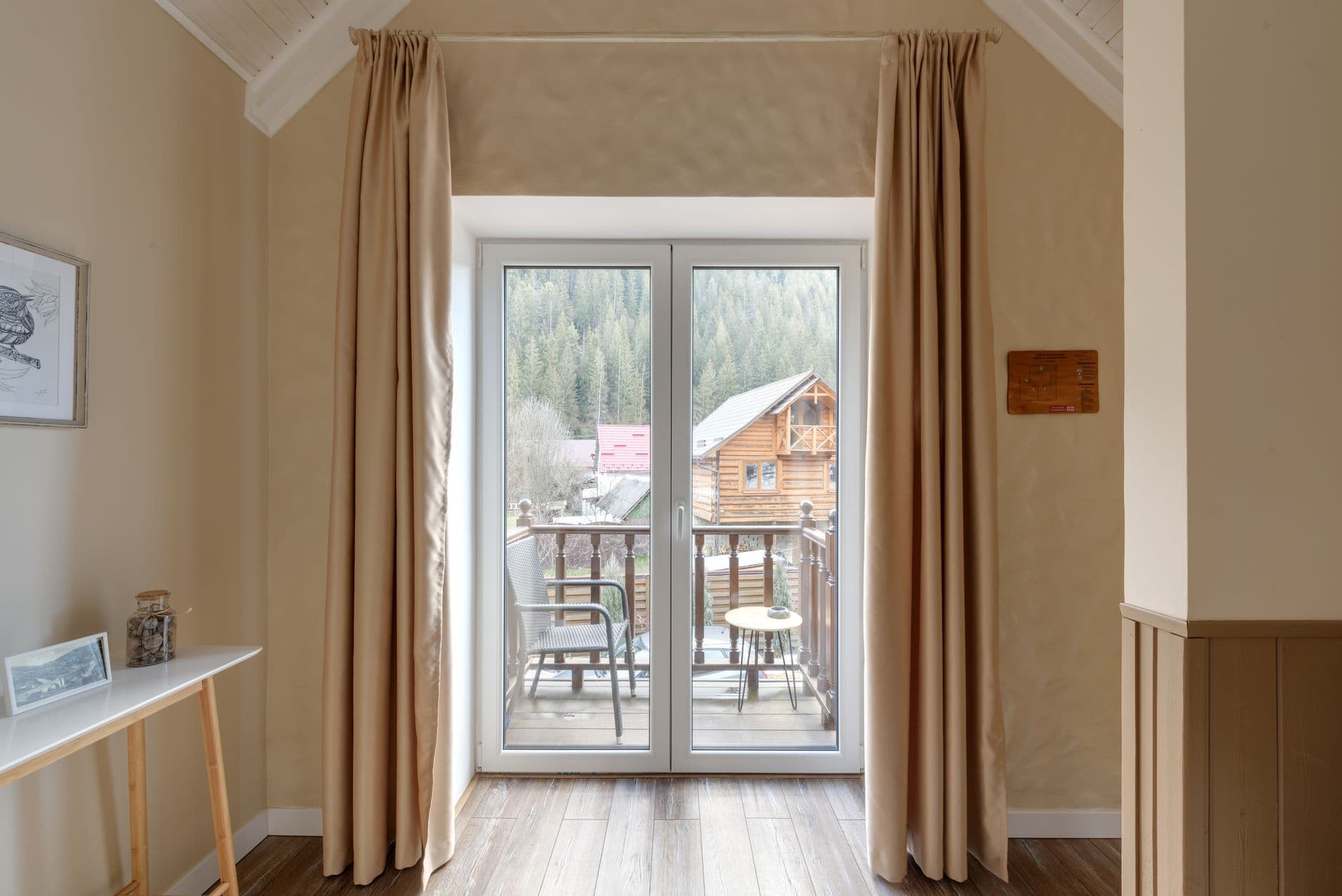 Puerta de balcón de dos hojas con cortinas beige y vistas a un bosque