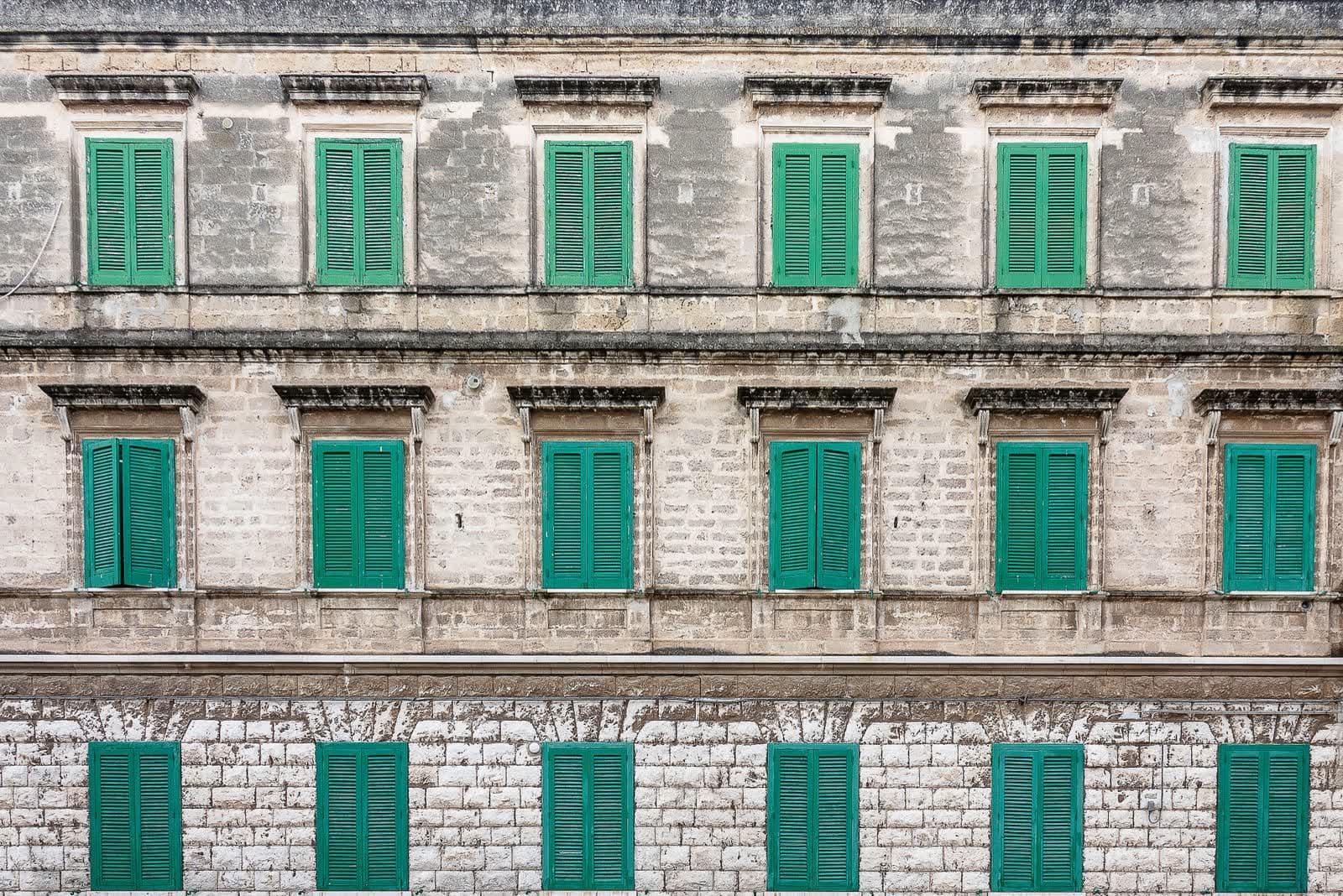 Fachada antigua de piedra con contraventanas de lamas verdes en tres alturas