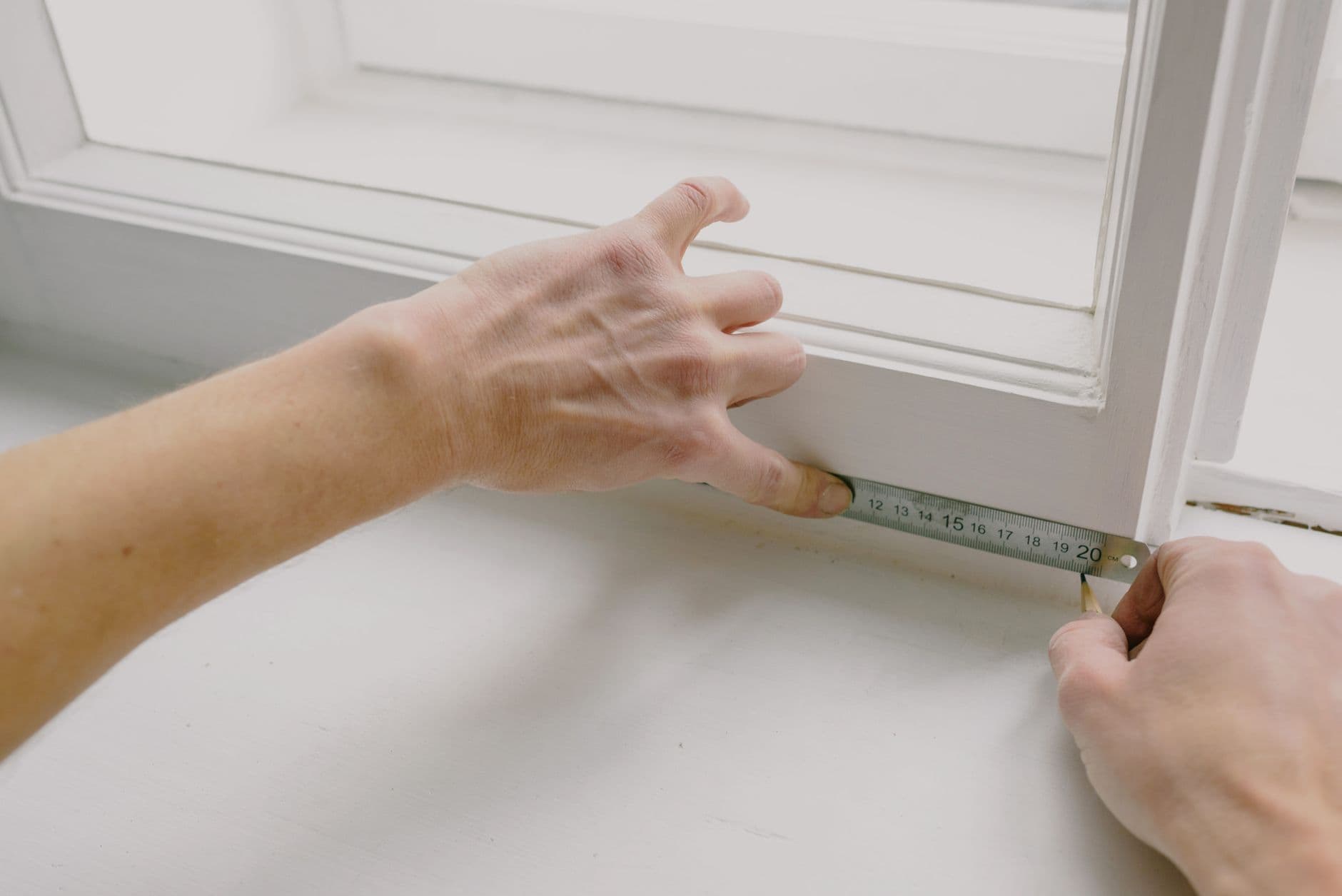 Dos manos midiendo con una regla metálica el interior de un marco de ventana