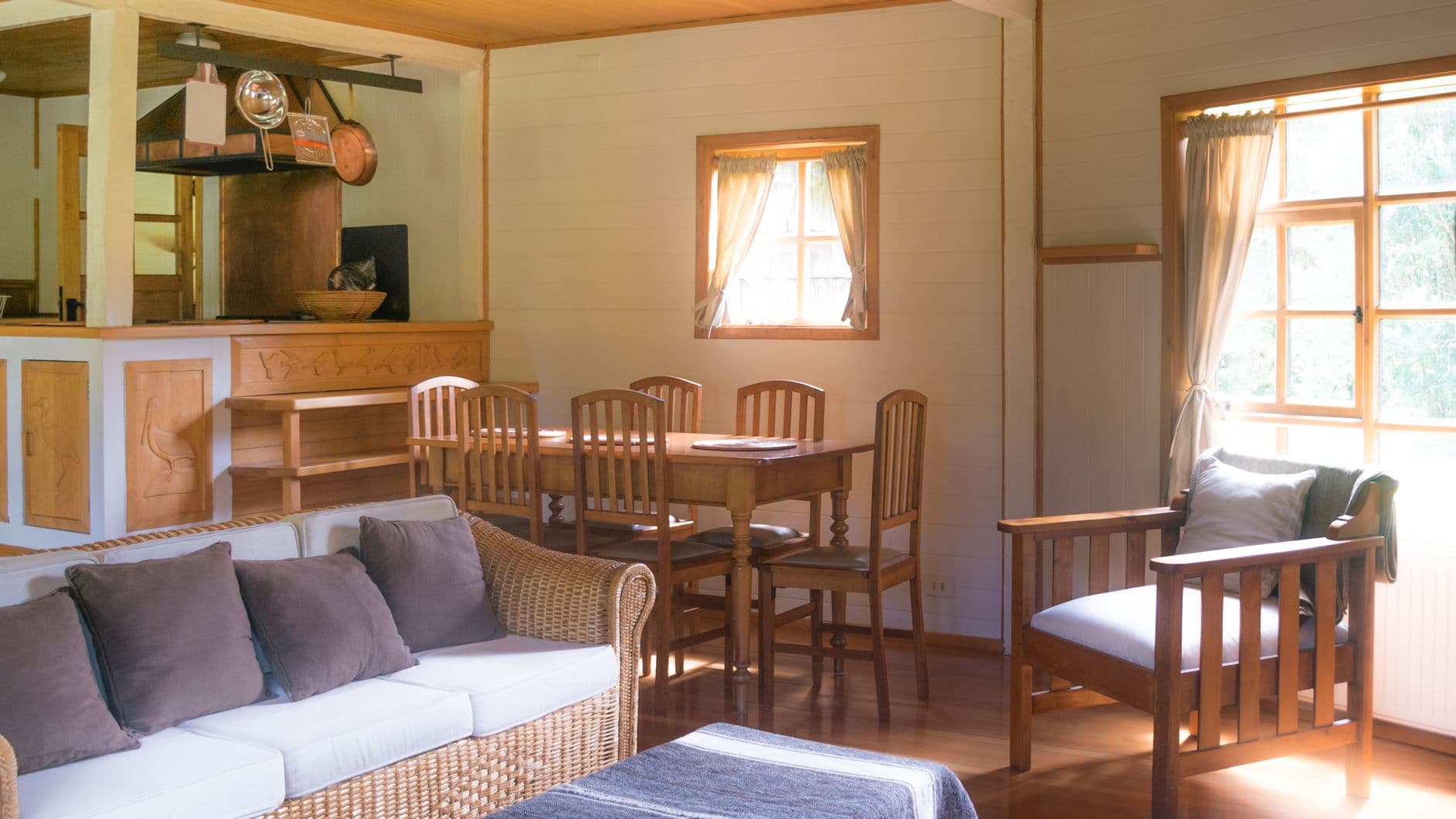 Salón comedor de una casa de madera con ventanas con visillos