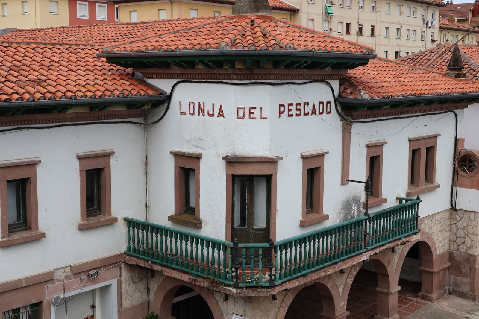 Edificio blanco con soportales, balcón corrido verde y tejado de teja