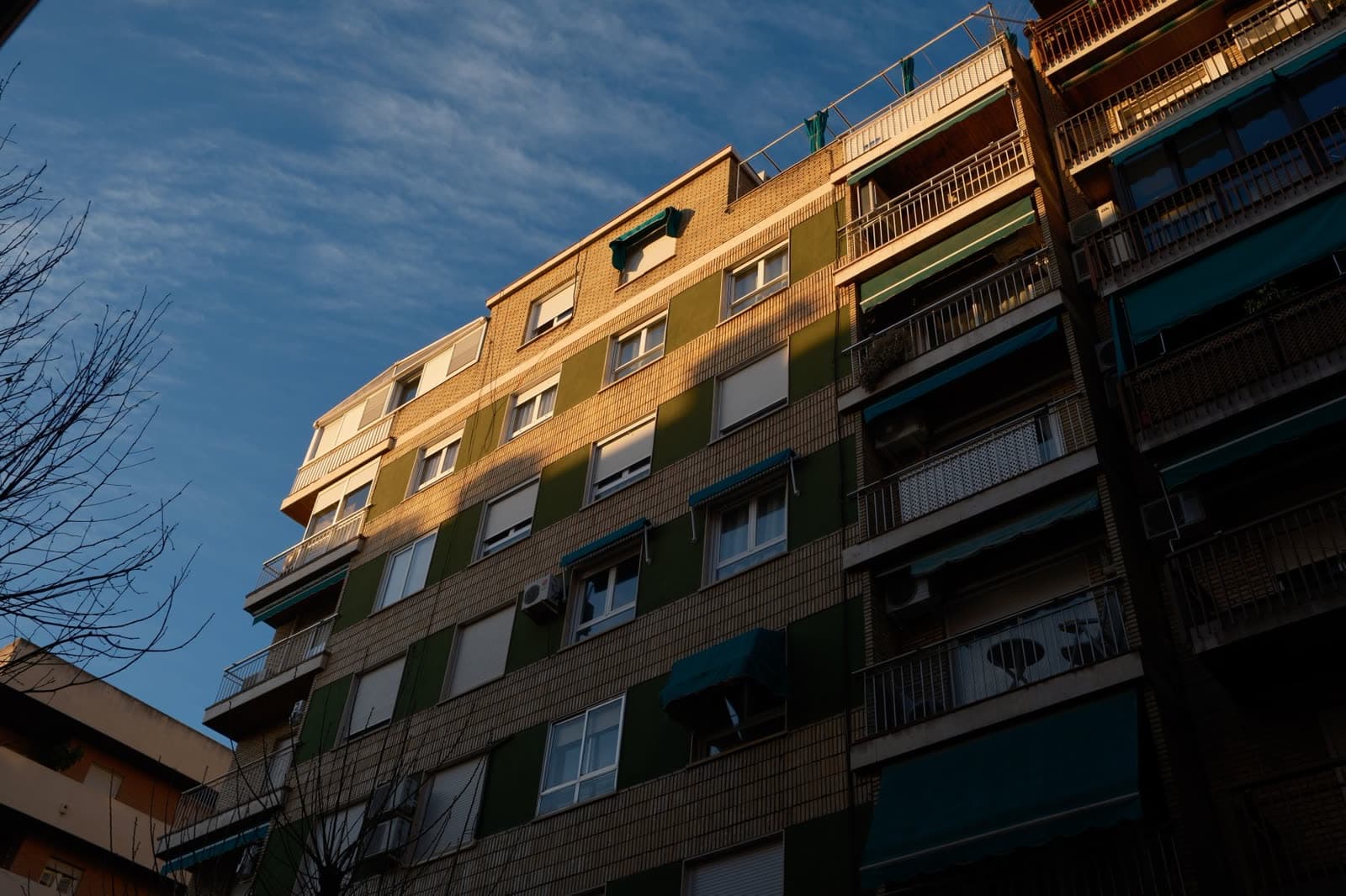 Bloque de viviendas con persianas y toldos bajo una luz baja y dorada de invierno