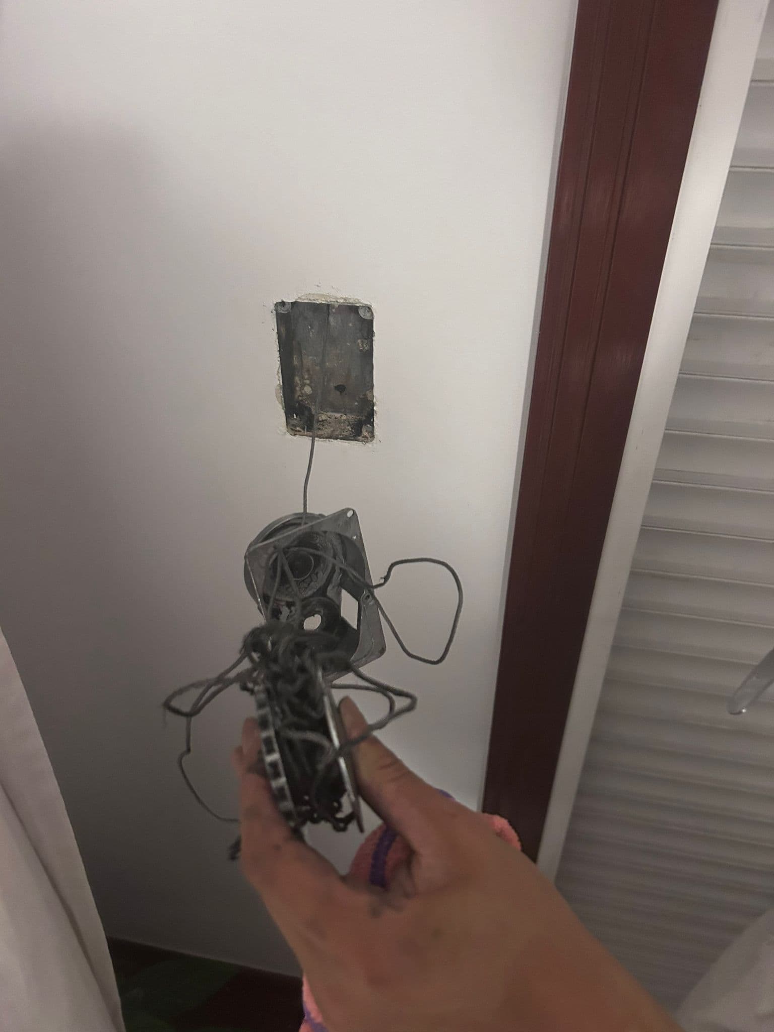 Mano sosteniendo el recogedor desmontado de una persiana, con el muelle y la cinta vieja enredados y llenos de suciedad, junto al hueco abierto de la caja empotrada en la pared