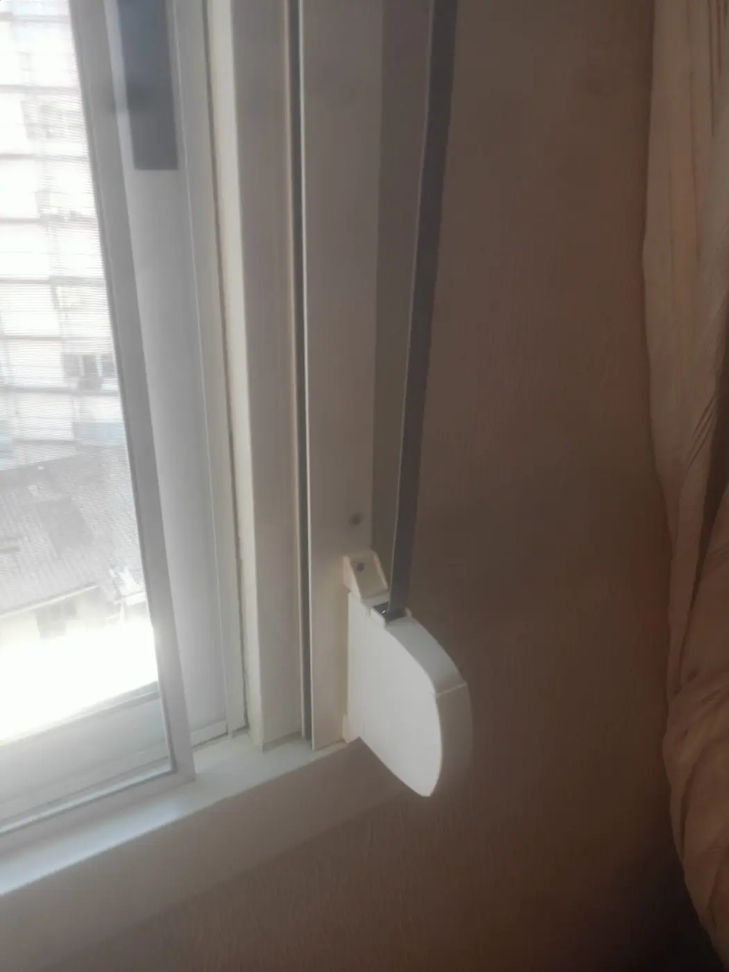 Detalle del recogedor de superficie blanco atornillado en la jamba interior de una ventana, con la cinta gris entrando en la guía